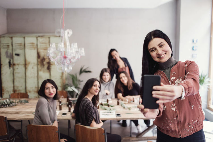 Smiling woman taking selfie with female colleagues at workshop