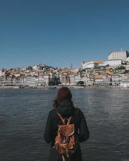 Rear view of woman standing by river against clear sky