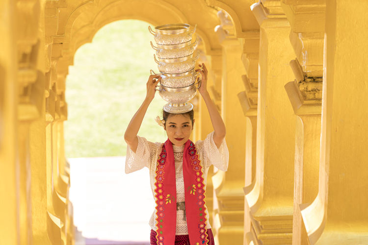 Portrait of smiling woman standing with bowls stack in temple