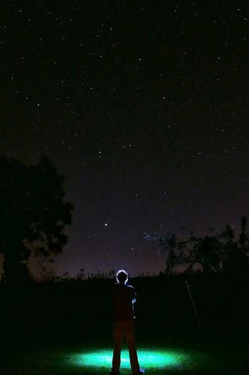 Rear view of man standing on illuminated field against constellation at night