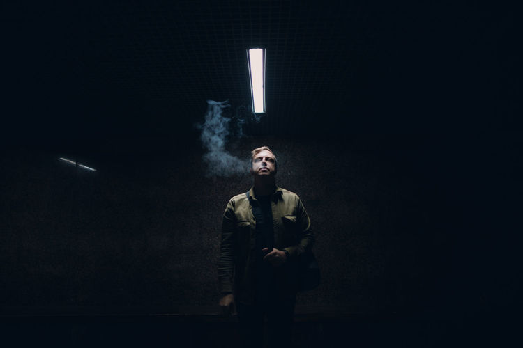 Portrait of young man smoking cigarette against black background