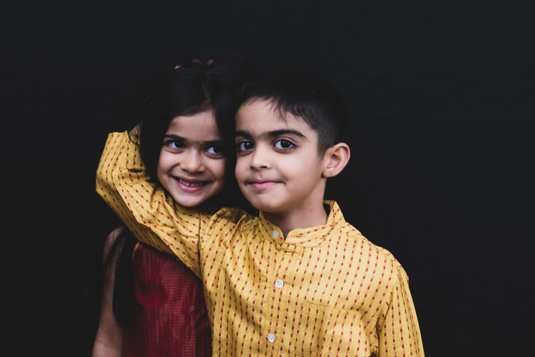Smiling siblings against black background