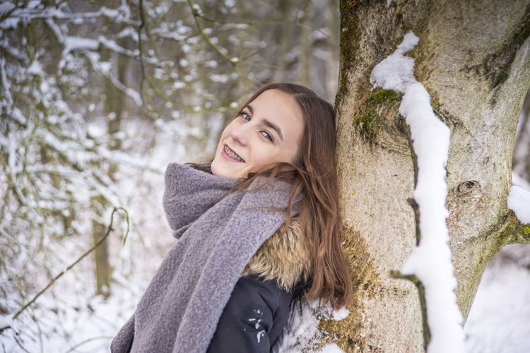 Portrait of smiling girl by tree on snow covered land