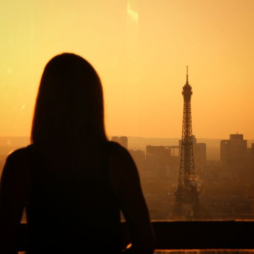 Rear view of silhouette woman looking eiffel tower in city at sunset