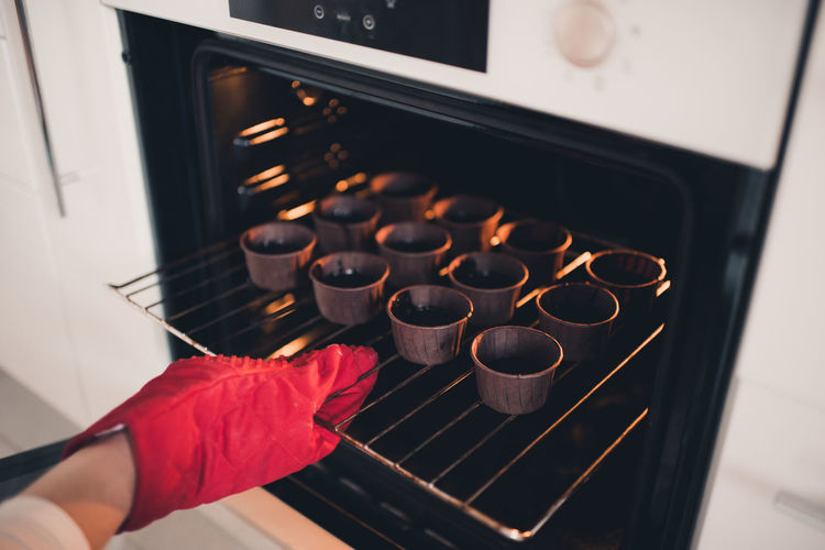 Woman put batter for chocolate cupcakes in oven in kitchen closeup. cooking time.