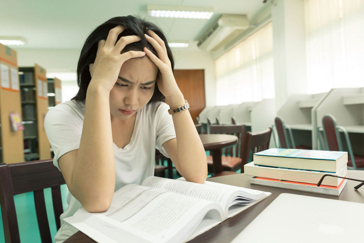 Close-up of stressed woman studying at library