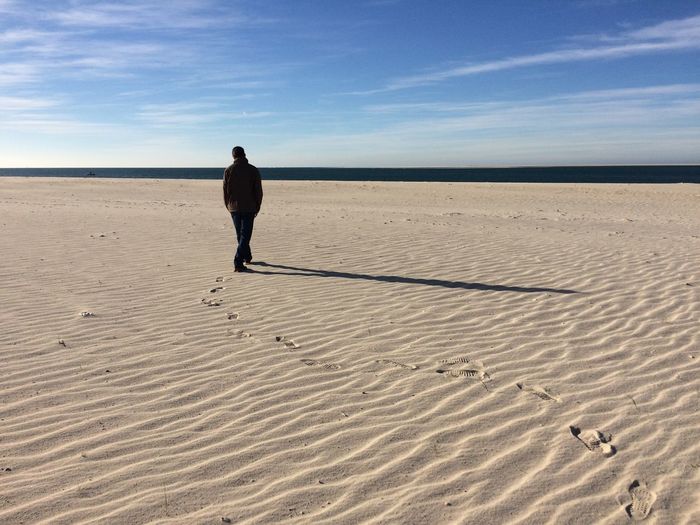 Rear view of man walking sandy beach against sky