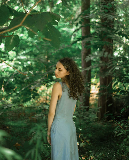 Young woman standing by tree in forest