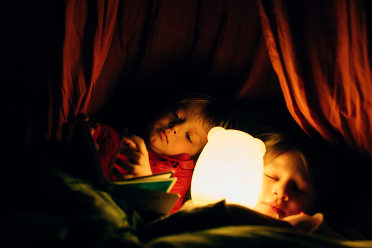 Child reading. kids lying in bed. boy looking at a book while her defocused sister sleeps 