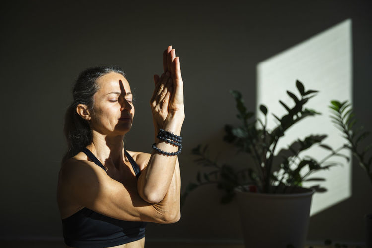 Yogini meditating with eyes closed in living room on sunny day