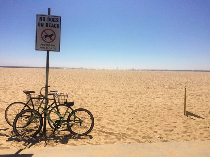Bicycle sign on sand against clear sky