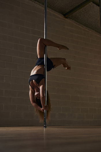 Graceful flexible woman dancing on pole and showing handstand during rehearsal in studio