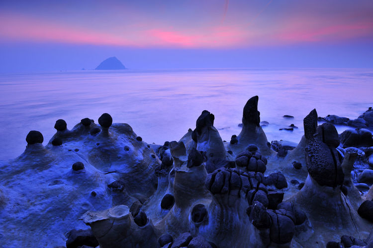 Rock formations by sea against sky at sunset