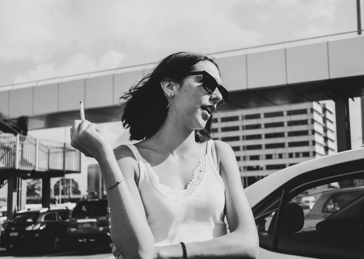 Woman wearing sunglasses smoking cigarette while standing outdoors