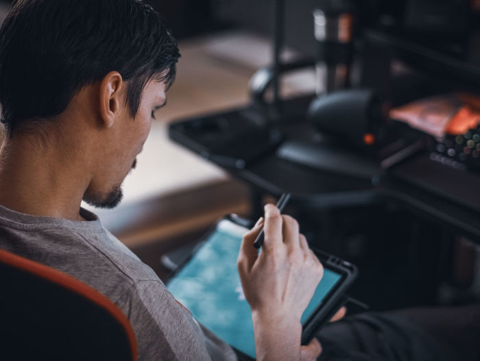 A caucasian guy sits in a work chair and holds a tablet with a black pen on his knees