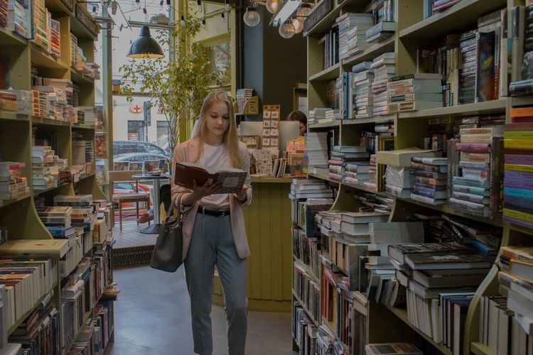 Young woman reading book while standing in bookstore