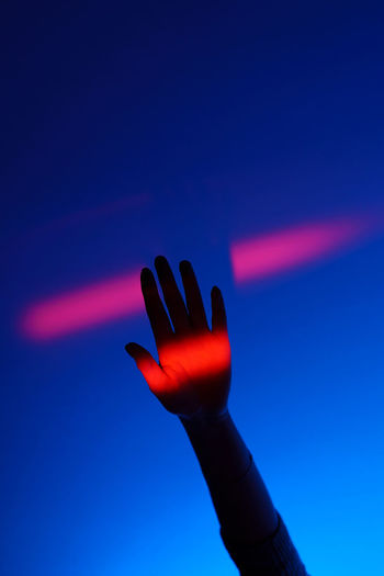 Woman arm gesturing with open hand over fashion blue background, neon red light on wrist and wall