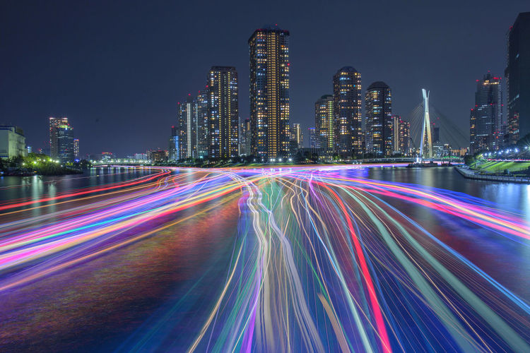 Light trails on road by illuminated buildings at night