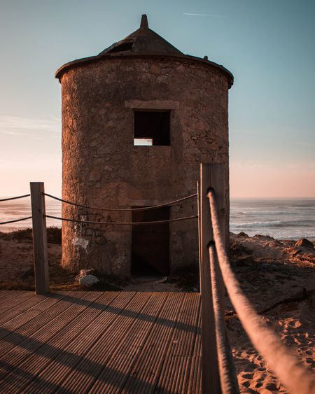 Built structure on beach against sky during sunset