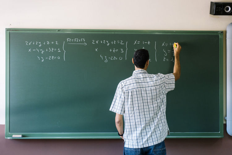 Math teacher writing formulas on chalkboard in classroom