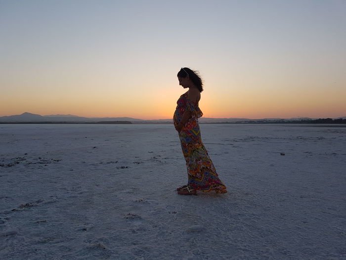 Side view of pregnant woman standing at salt flat against sky