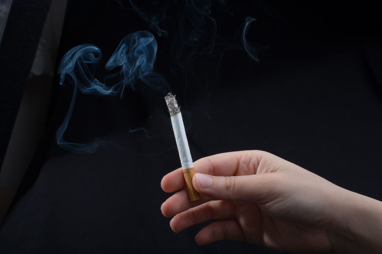Cropped hand of person holding cigarette against black background