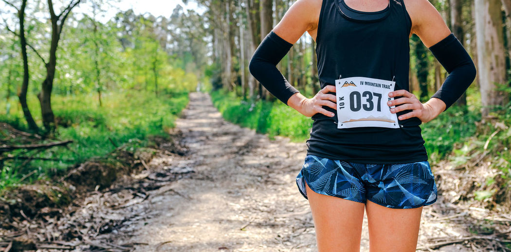 Midsection of woman standing with marathon bib in forest