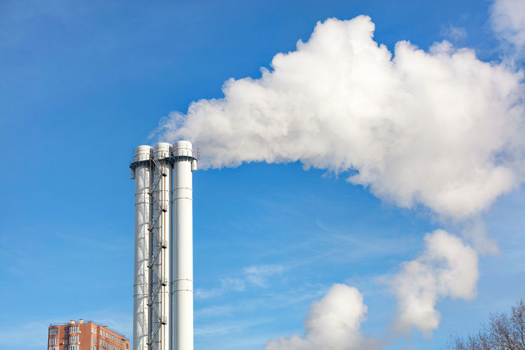 The high triple white chimney of the chp plant emits smoke and steam into the atmosphere. 