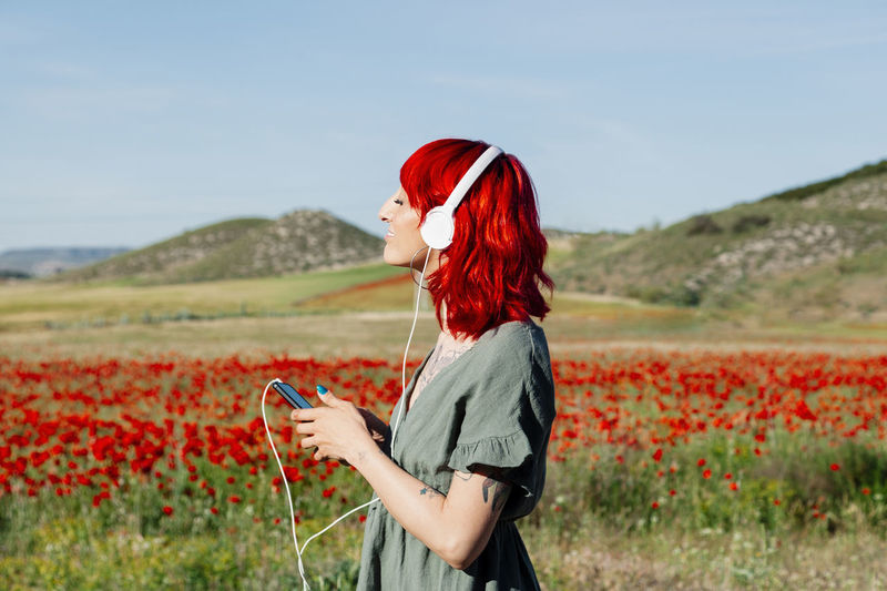 Young woman with eyes closed listening music on field during sunny day