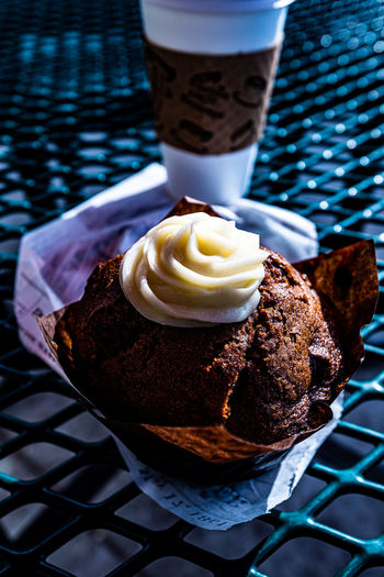 Coffee and a carrot cake muffin in rustic brown paper  topped with a swirl of cream cheese frosting