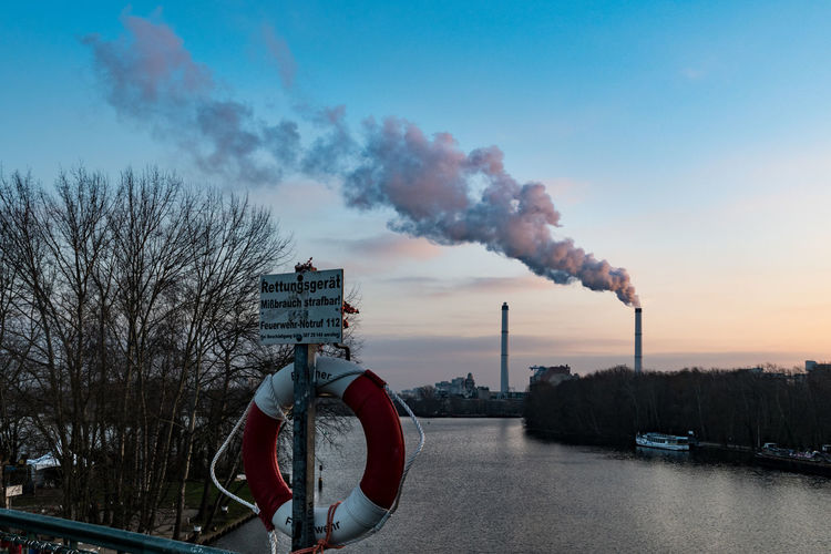 Smoke emitting from chimney by river against sky