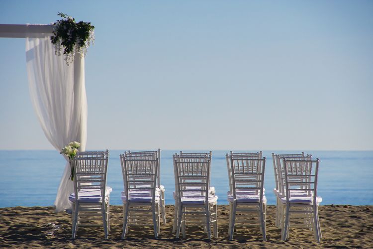 Empty chairs on sand at beach against clear sky