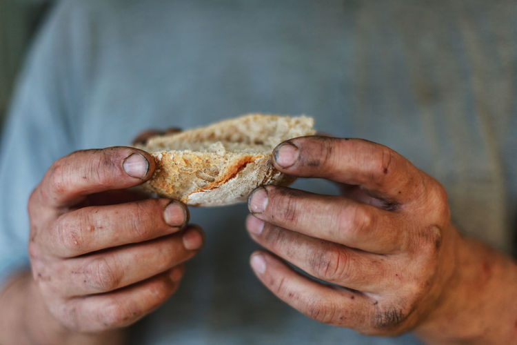 Piece of freshly baked bread in dirty hands of hard working man