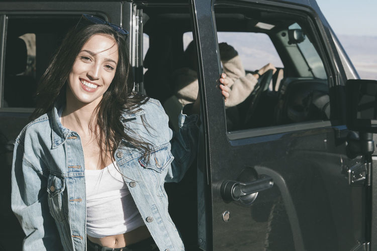 Portrait of confident young woman while friend sitting in off-road vehicle during sunny day