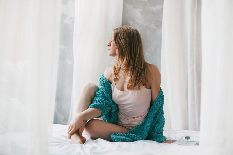 Cute girl sitting cross-legged on the bed in the morning. young woman in pajamas