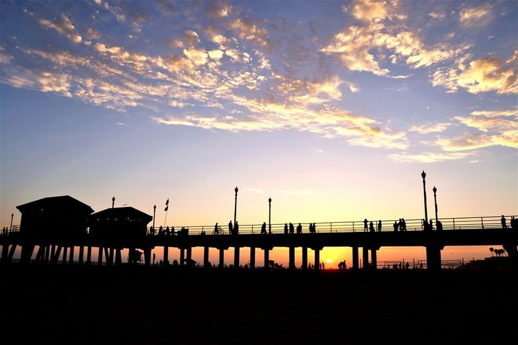 Silhouette of people walking on pier at sunset