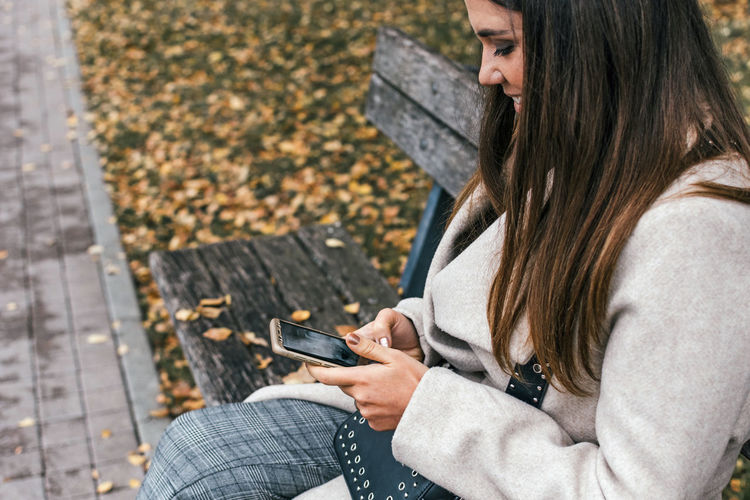 Woman using phone while sitting on bench at park