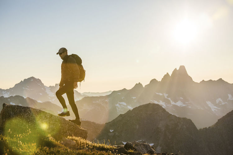 Backpacker hiking on high mountain ridge while sun sets over mountain.