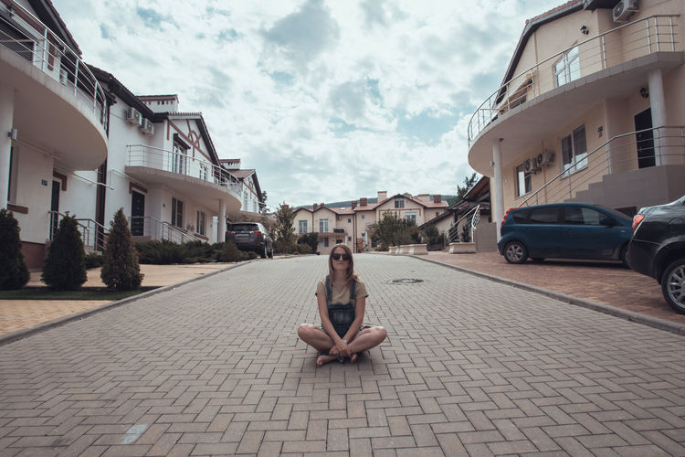 Woman sitting on street in city against sky