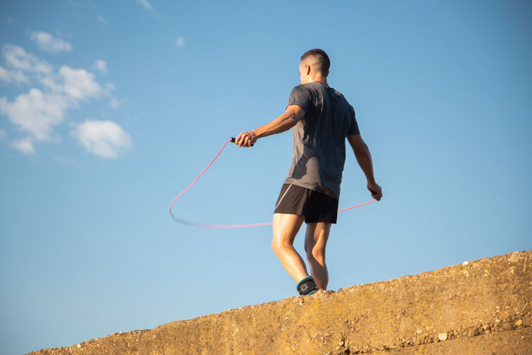 Low angle view of man exercising against blue sky