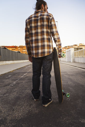 Rear view of man with skateboard standing in city against sky