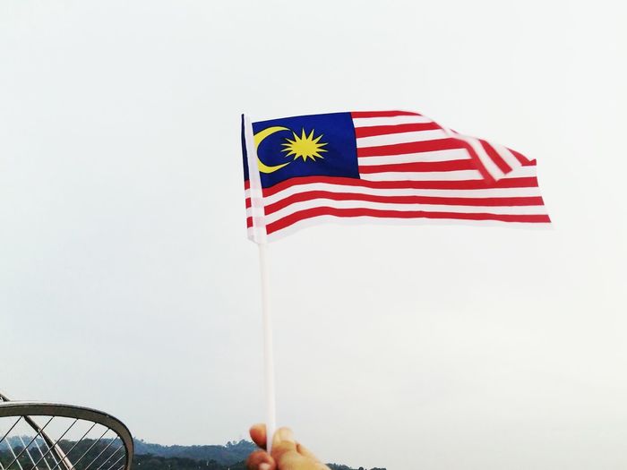 Cropped hand holding malaysian flag against clear sky