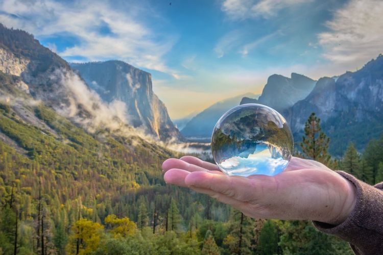 Close-up of hand holding landscape against mountain range