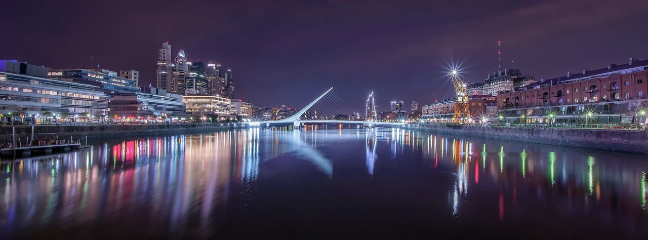 Panoramic shot of puente de la mujer over river in illuminated city at night