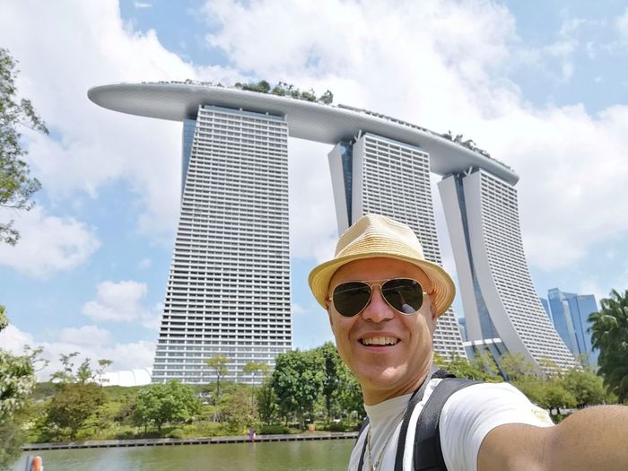 Portrait of smiling man wearing sunglasses against marina bay sands and sky