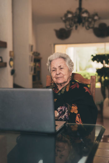 Elderly female with short gray hair sitting on chair making video call via netbook at home