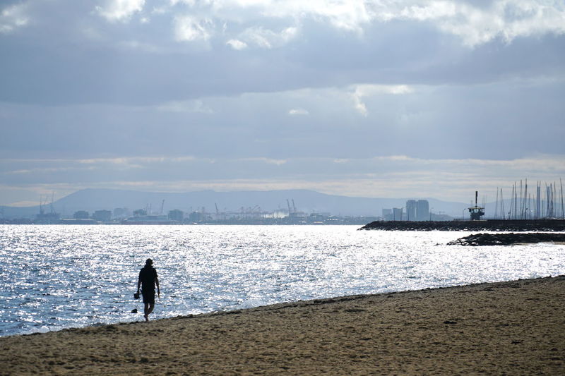 Silhouette man walking on beach against sky.