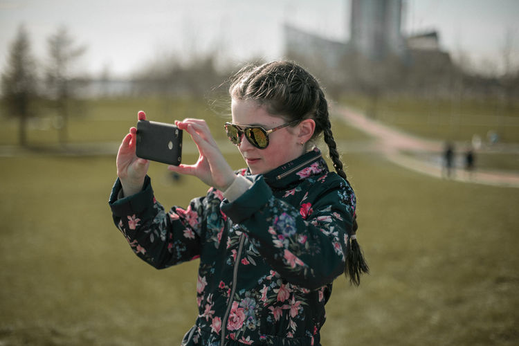 Girl holding camera while standing on field