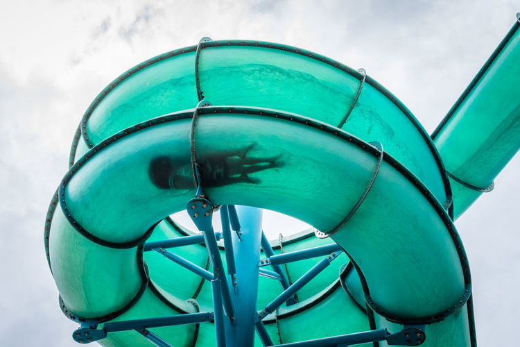 Low angle view of turquoise water slide against cloudy sky