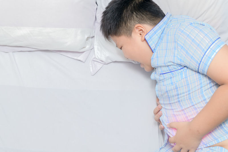 Boy with stomachache lying on bed at home